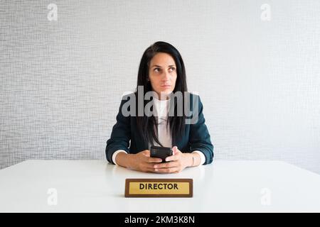 Junge, brünette Geschäftsfrau in einer kaukasischen Firma, leitende Direktorin im Büro, nachdenklicher Unternehmer, der ein Telefon hält, trifft Entscheidungen, bevor Text oder Modell isoliert überlegt werden Stockfoto