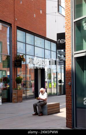 Ein Mann liest auf einer Bank im Old Market Shopping Centre, Hereford, Herefordshire Stockfoto