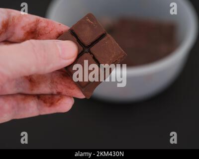 Ein Mann, der ein Stück geschmolzene Schokolade aus einer Schüssel Schokolade nimmt. Schließen. Stockfoto