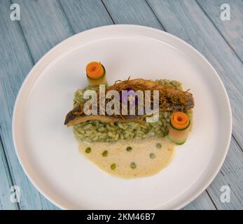 Rezept für gebratenes Seebarschfilet mit Kräuterrisotto, Weißweinsauce, Fresch-Creme, Karottenrolle und Zucchini-Streifen Stockfoto