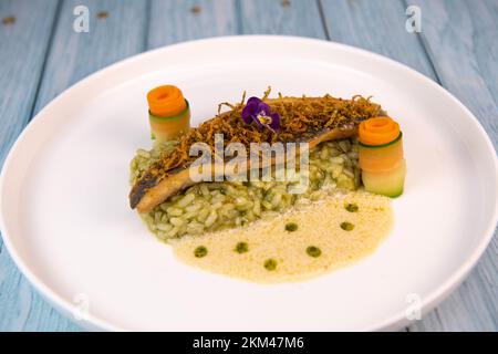 Rezept für gebratenes Seebarschfilet mit Kräuterrisotto, Weißweinsauce, Fresch-Creme, Karottenrolle und Zucchini-Streifen Stockfoto