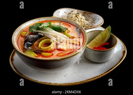 Tom Yum Suppe mit Shrimps, Muscheln und Tintenfisch, auf schwarzem Hintergrund Stockfoto