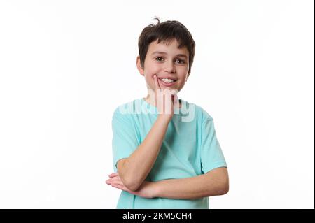 Ein glücklicher Junge, der seine Hand am Kinn abdrückt und süß lächelt, mit Bedacht in die Kamera schaut, isoliert über weißem Hintergrund Stockfoto