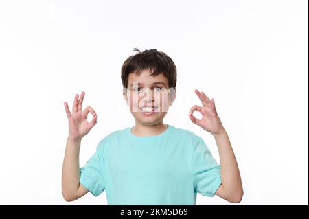 Ein glücklicher weißer Junge zeigt ein OK-Schild, das in die Kamera schaut, isoliert auf weißem Hintergrund. Kostenlose Werbefläche Stockfoto