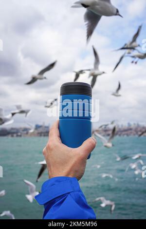 Nahaufnahme eines handgehaltenen Thermoreisetassens mit Möwen im Hintergrund. Stockfoto