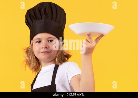 Lustiger Kinderkoch mit Kochplatte. Kinderkoch. Kindergarderobe und Kochmütze für die Zubereitung von Speisen, Studioporträt. Stockfoto