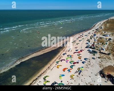 Blick von oben auf helle farbenfrohe Drachen, die am windigen Tag am Kitesurfplatz am Strand geparkt sind. Viele Fallschirme zum Kiteboarden liegen am Ufer Stockfoto