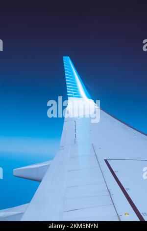 Aus dem Fensterplatz des Flugzeugs zu schauen und die Flügelspitze auf dem Flügel des Flugzeugs zu sehen. Mit tiefblauem Hintergrund. Stockfoto