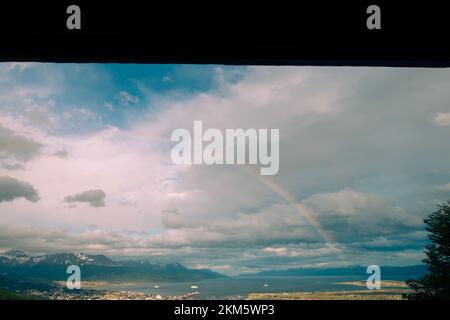 Blick auf die Berge rund um die Stadt Ushuaia. Mit einem Regenbogen über der Stadt an einem Sommertag. Stockfoto