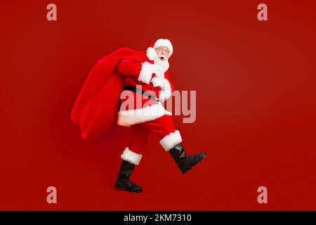 Volle Länge Körpergröße Profil Seitenansicht seiner HE Nette lustige fröhliche erstaunt weißhaarige Santa trägt großen großen Sack Benutzerdefinierte Tradition isoliert hell Stockfoto