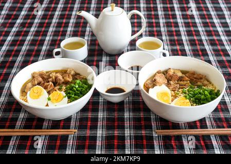 Japanische Ramen mit Huhn und Sojasoße auf dem Tisch mit Teekanne und grünem Tee Stockfoto