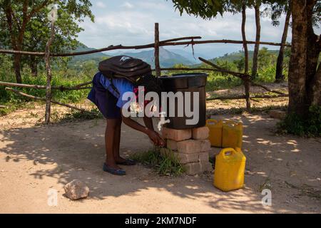 Junge Studentin wäscht sich vor dem Unterricht die Hände mit einem Gallonen-Wasserspender mit Hahn Stockfoto