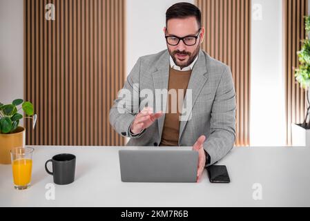 Ehrgeiziger erwachsener Geschäftsmann mit Brille, der ein Online-Gespräch mit seinen Geschäftspartnern führt. Stockfoto