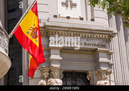 Madrid, Spanien - 20. Juni 2022: Spanische Flagge im Vordergrund und Eingang des Madrider Hauptquartiers des Cervantes-instituts, eines instituto, das di Stockfoto