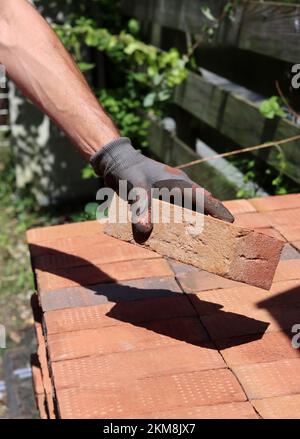 Männerhand mit rotem Ziegel. Bau- und Baukonzept. Hausrenovierung im Gange. Stockfoto