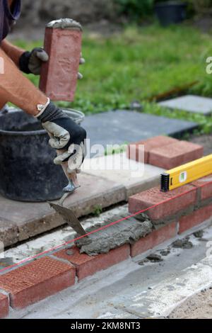 Bauarbeiten im Gange. Männlicher Baumeister, der mit roten Ziegeln arbeitet. Nahaufnahme der Mauerwand. Stockfoto