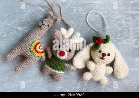 Weihnachtsgehäkelte. Süßes Häkelspielzeug Foto von oben. Wunderschöne Amigurumi-Tiere. Hausgemachte Weihnachtsgeschenke. Grauer Hintergrund mit Kopierbereich. Stockfoto