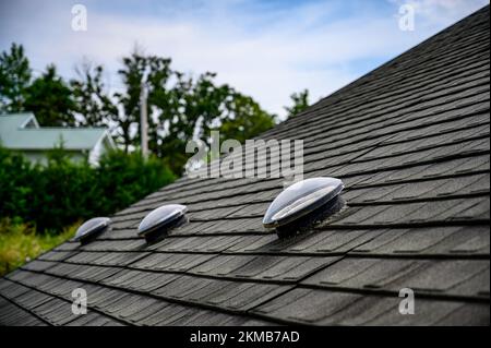 Kuppelförmiges Sonnenröhren-Oberlicht auf Asphalt-Schindeldach Stockfoto