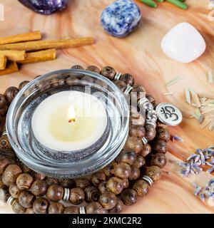 Selbsthilfe, heilende Komposition mit Rosenkranzperlen, Chakrasteinen, Sandelholzstangen und Kerzen auf einem pinkfarbenen Marmorpodium. Konzept der Entspannung zu Hause, en Stockfoto