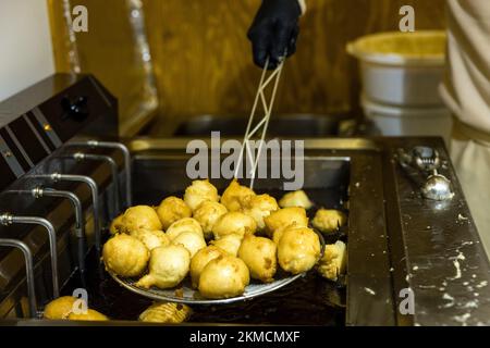 Naumburg, Deutschland. 26.. November 2022. Ein Mann schöpft Mutzen - ein fettes Gebäck - aus heißem Fett auf dem Naumburger Weihnachtsmarkt. Neben dem Weihnachtsmarkt haben zahlreiche Institutionen sowie Unternehmen und Privatpersonen ihre Höfe am ersten Adventswochenende in Naumburg eröffnet. Besucher können manchmal Bereiche sehen, die ansonsten nicht sichtbar sind. Kredit: Frank Hammerschmidt/dpa/Alamy Live News Stockfoto