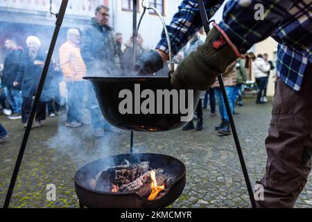 Naumburg, Deutschland. 26.. November 2022. Ein Mann rührt sich in einem Topf, der über einem Holzfeuer hängt. Zahlreiche Institutionen sowie Unternehmen und Privatpersonen öffnen ihre Höfe am ersten Adventswochenende in Naumburg. Besucher können Bereiche sehen, die ansonsten nicht sichtbar sind. Kredit: Frank Hammerschmidt/dpa/Alamy Live News Stockfoto