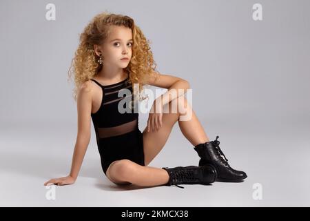 Hübsche Turnerin in einem schwarzen Sportbadeanzug und Stiefeln auf grauem Hintergrund. Stockfoto