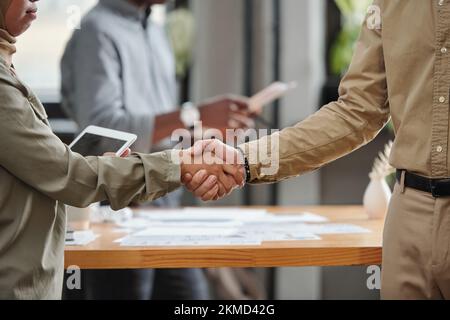 Nahaufnahme des Händedrucks zweier junger interkultureller Geschäftspartner, die sich gegenseitig zur Unterzeichnung eines neuen, vielversprechenden Vertrags beglückwünschen Stockfoto