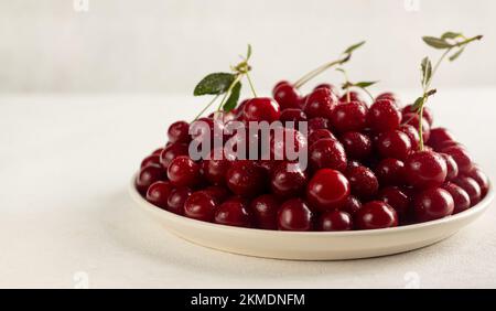 Reife Kirschen auf einem Teller auf hellem Hintergrund, leckere, süße Beerennaturprodukte ohne Pestizide Stockfoto