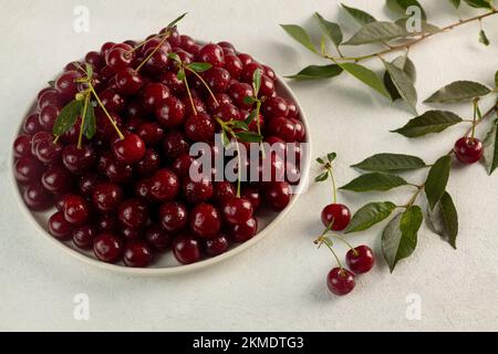 Reife Kirschen auf einem Teller auf hellem Hintergrund, leckere, süße Beerennaturprodukte ohne Pestizide Stockfoto