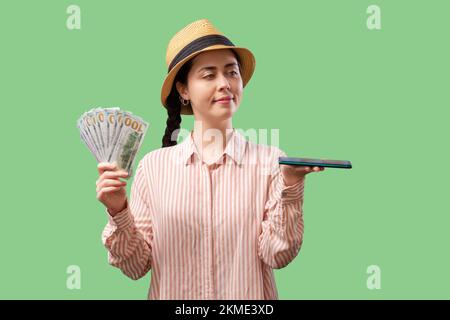 Investierende App. Eine hübsche weiße Frau hat ein Telefon und einen Fan von Dollarscheinen. Grüner Hintergrund. Konzept von Börse und digitalem Geld. Stockfoto