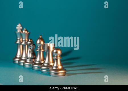 Silberne Schachfiguren stehen in einer Reihe auf blauem Hintergrund. Stockfoto