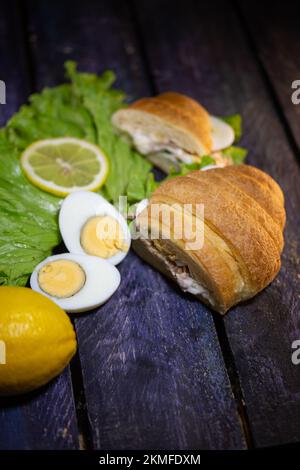 Frische Croissants mit Thunfisch, Salat und Ei auf Holzhintergrund. Stockfoto