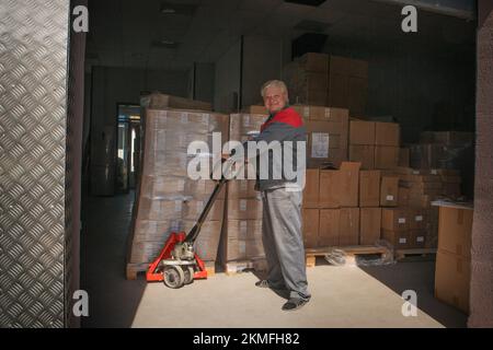 Ein Lader rollt einen Wagen in einem Lagerhaus zwischen vielen Kisten. Hochwertiges Foto. Stockfoto