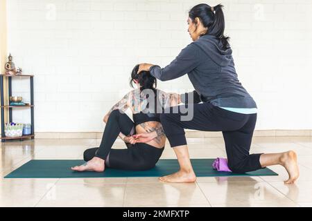 Yoga-Lehrerin, die die Haltung eines Schülers korrigiert, der eine ardha matsyendrasana macht Stockfoto