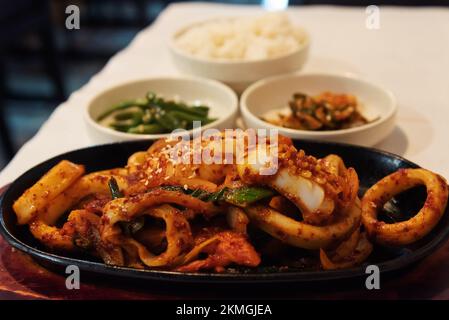 Gebratener Tintenfisch, Reis, Kimchi und Gemüse als Beilagen in einem authentischen koreanischen Restaurant, das hausgemachte traditionelle, einfache Bio-Gerichte serviert. Stockfoto