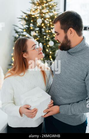 Süßes, junges Paar, das Weihnachtsgeschenke gegen Weihnachtsmorgen tauscht Stockfoto