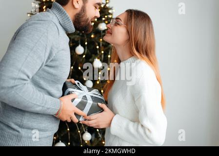 Süßes, junges Paar, das Weihnachtsgeschenke gegen Weihnachtsmorgen tauscht Stockfoto