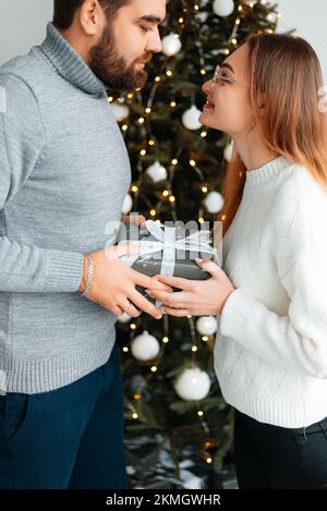 Süßes, junges Paar, das Weihnachtsgeschenke gegen Weihnachtsmorgen tauscht Stockfoto