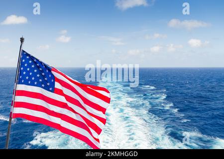 Die Flagge der USA auf einem Kreuzfahrtschiff mit Wache oder Pfad auf der Meeresoberfläche Stockfoto