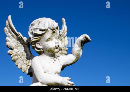 Traurige Hüter-Engel-Skulptur mit offenen langen Flügeln über dem Rahmen, entsättigt vor einem hellen weißen Himmel. Die traurige Ausdrucksskulptur mit Blick nach unten Stockfoto