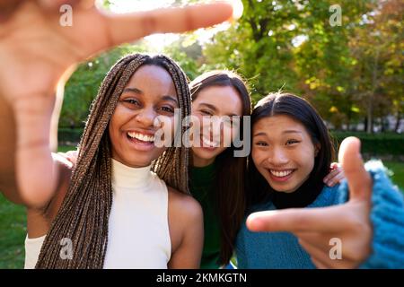 Drei gemischte Freunde machen Selfie, machen Handgesten im Naturpark, schauen in die Kamera Stockfoto