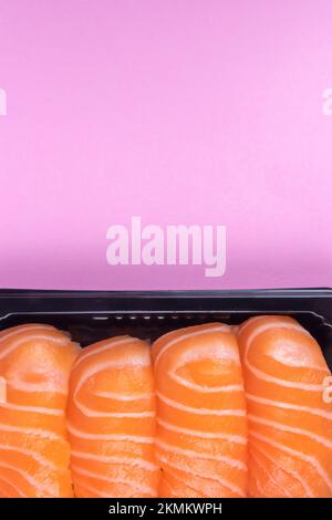 Lachs-Sushi in schwarzem Tablett auf rosa Hintergrund. Draufsicht mit Kopierbereich. Stockfoto
