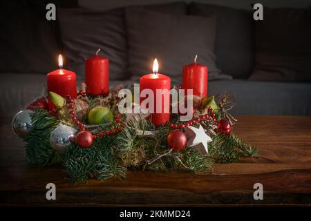 Adventskranz mit zwei brennenden roten Kerzen und Weihnachtsdekoration auf einem Holztisch vor der Couch, festliches Heimdekor für den zweiten Sonntag, Stockfoto
