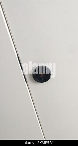 Abstrakte, hochpräzise Nahaufnahme mit einem glänzenden Metallgeländer und einer runden, schwarzen Befestigung an einer weißen Wand. Stockfoto