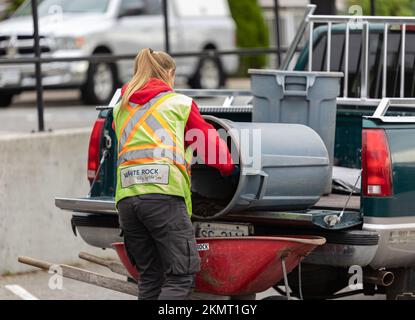 Wartungshelferin, die Schmutz sammelt. Straßenreiniger trägt Sicherheitsweste. Weibliche Mitarbeiterin in orangefarbener Kleidung reinigt Stadtgebiet-White Rock B. Stockfoto