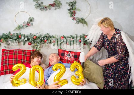 Schönes Paar liegt im Bett und plant, ein Baby zu haben. Weihnachten und frohe Neujahr mit den Zahlen 2023 Stockfoto