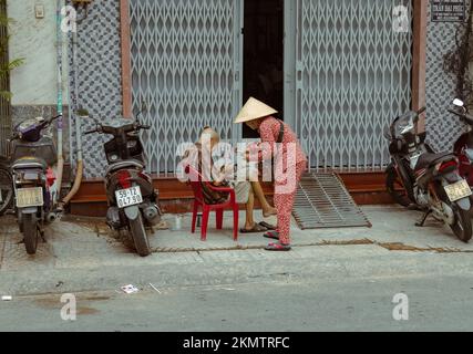 Ho-Chi-Minh-Stadt, Vietnam - 8. November 2022: Eine ältere Frau in traditioneller vietnamesischer Kleidung und ohne Kopfschmuck verkauft Lotteriekarten an einen alten Mann Stockfoto