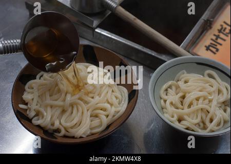 Suppe über Schüsseln mit kauenden udon-Nudeln bei Chikusei Udon, Takamatsu, Japan. Stockfoto