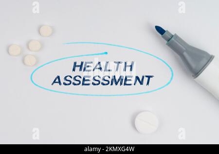 Medizin und Gesundheitskonzept. Auf einem weißen Blatt Papier, Tabletten, einem Marker und einer Aufschrift - GESUNDHEITSBEURTEILUNG durch ein gezogenes Oval angezeigt. Stockfoto
