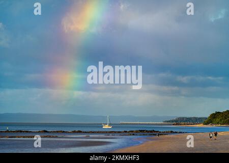Regenbogen über Hervey Bay mit Segelboot und Urangan Pier in der Ferne. Hervey Bay Queensland, Australien Stockfoto